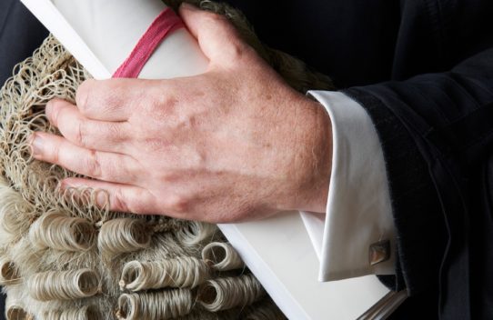 A close up shot of a judge holding a scroll and periwig