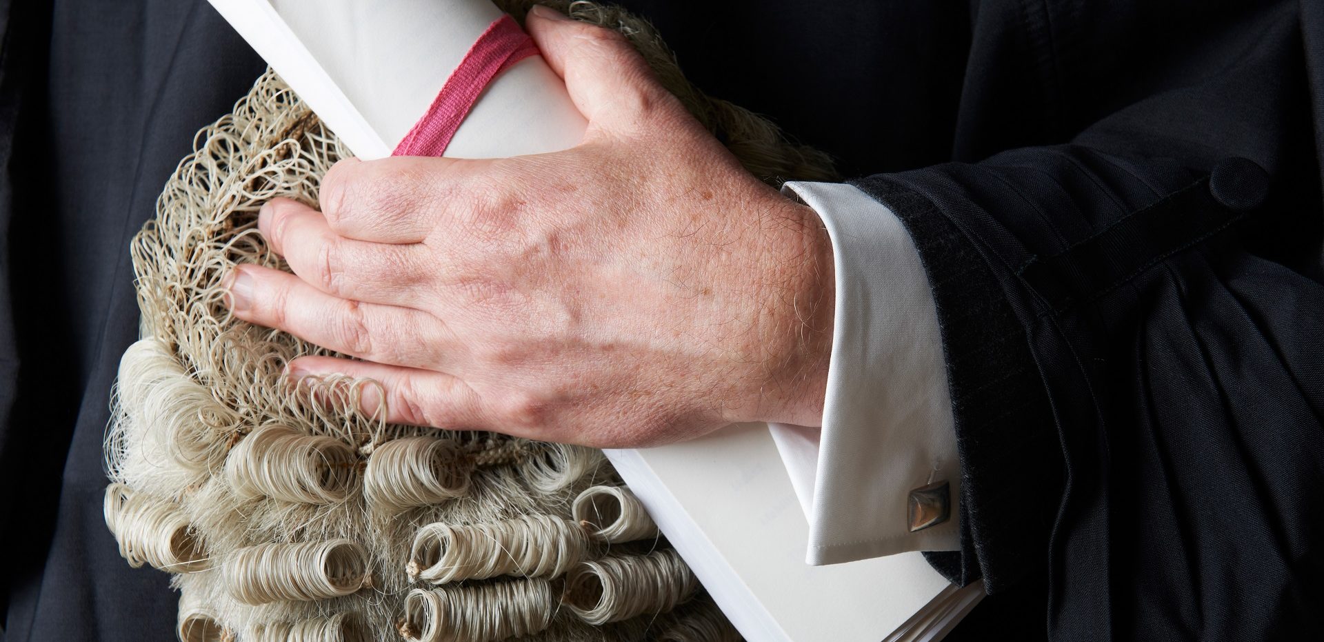 A close up shot of a judge holding a scroll and periwig